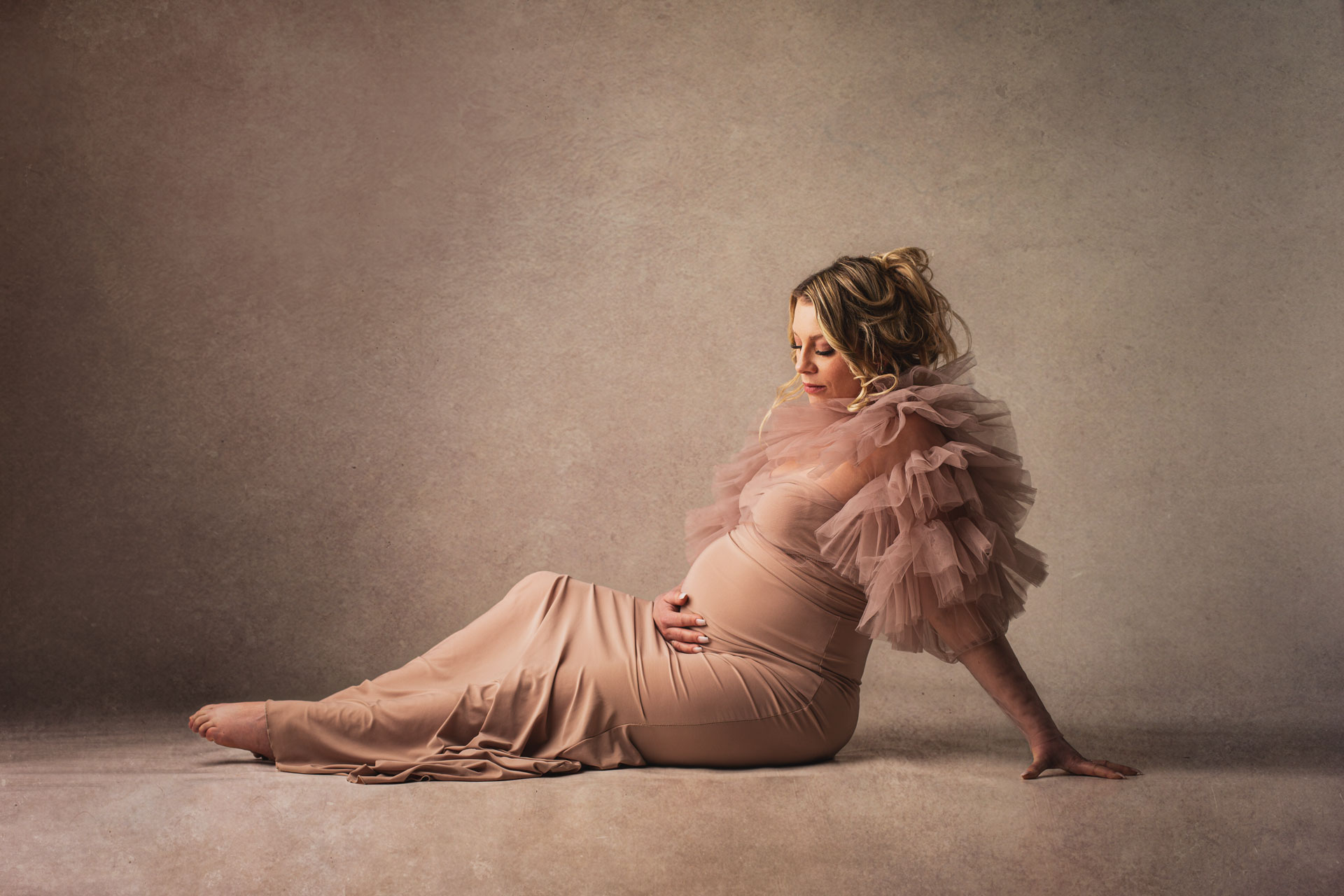 schwangere Frau im beigen Kleid mit Rüschenärmel sitzt auf dem Boden