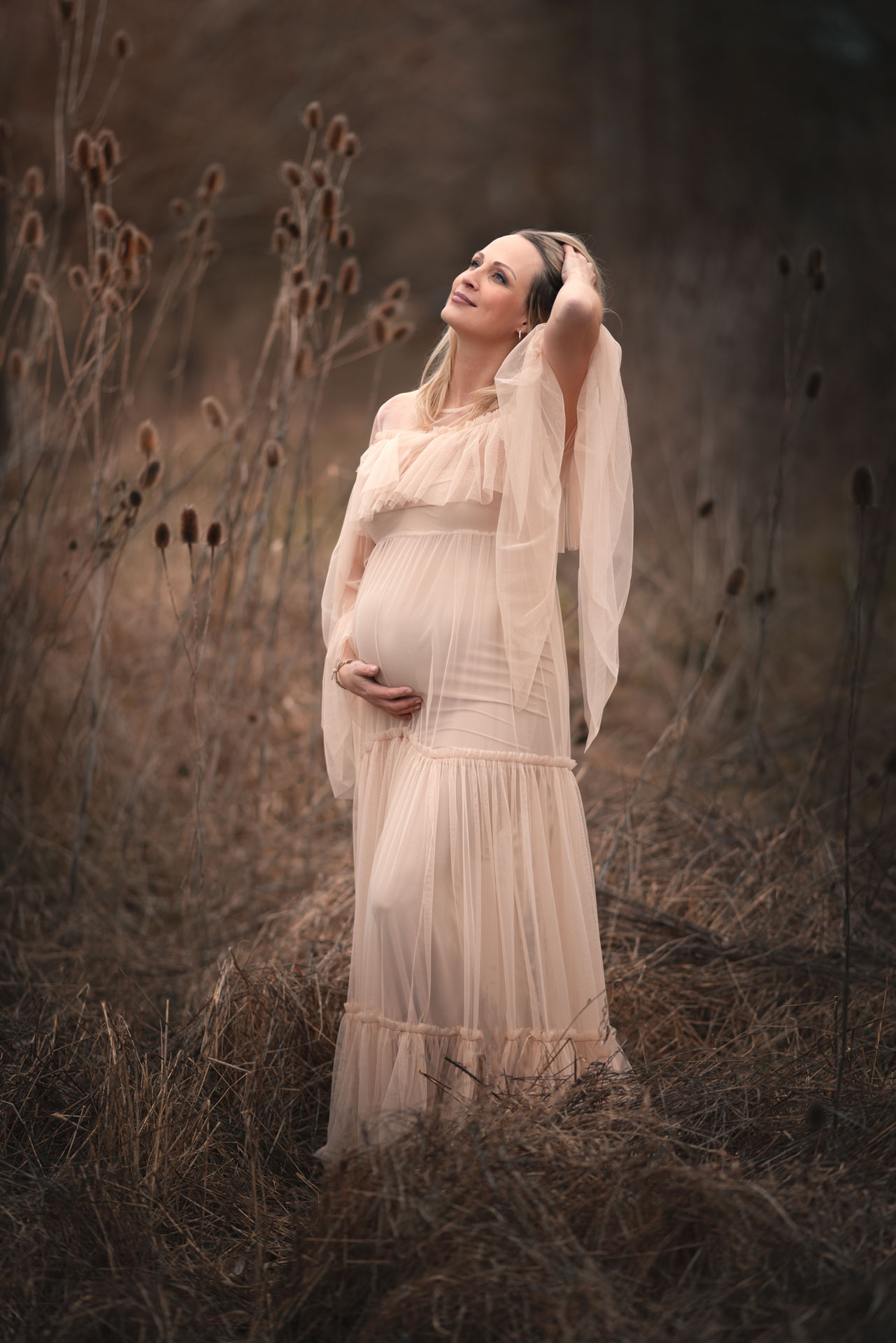 Schwangere Frau im weißen Kleid steht im Studio vor blumigem Hintergrund