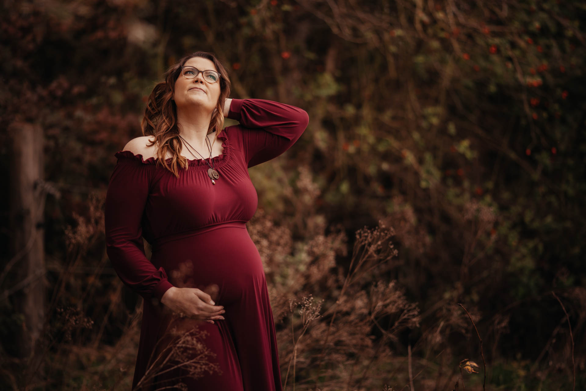 schwangere Frau im petrolfarbenen Samtkleid steht zwischen Disteln im hohen trockenen Gras