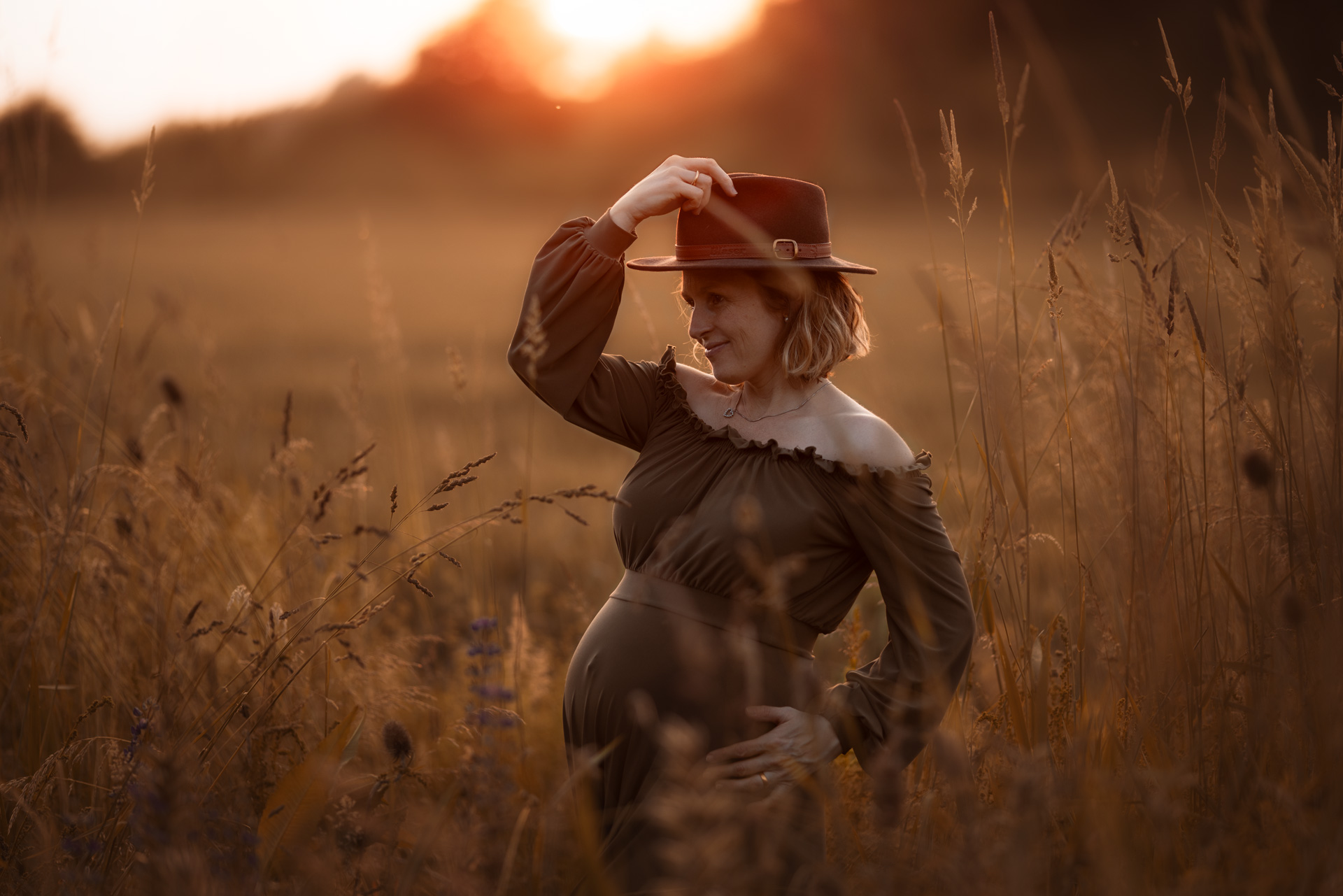 26-Babybauchshooting schwangere Frau im petrolfarbenen Samtkleid steht zwischen Disteln im hohen trockenen Gras