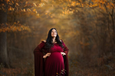 Babybauchfotografie im roten Kleid mit rotem Umhang im Herbstwald