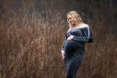 Babybauchfotografie im blauen Samtkleid im verdörrtem hohen Gras