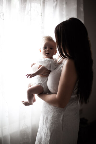 Mutter steht vor einem FGenster und hält ihr Baby vorm Bauch.